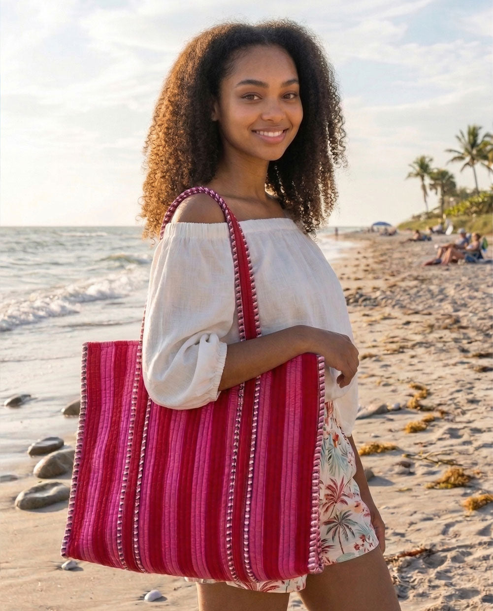 Woman holding a red and pink striped bag on a beach